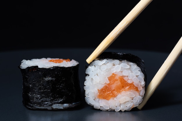 Sushi roll with salmon on a black background Wooden chopsticks hold sushi roll