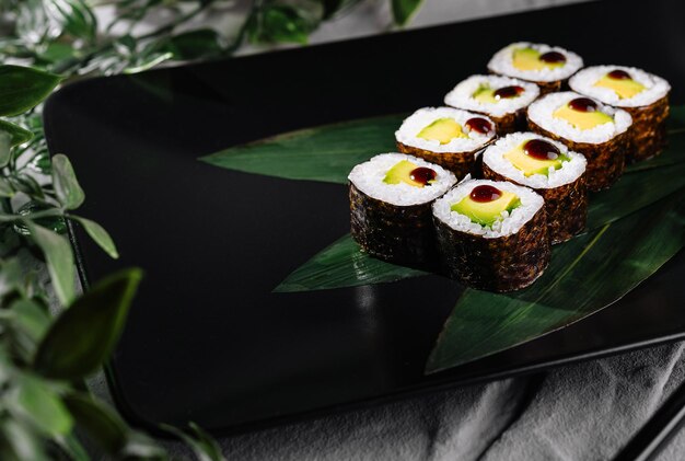 Photo sushi rolls garnished with wasabi and ginger on a modern black plate botanical backdrop