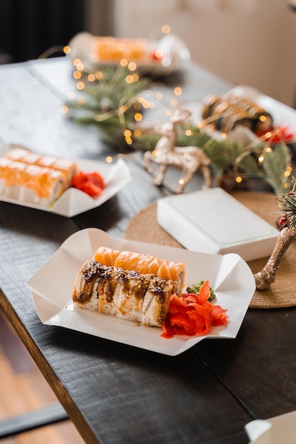 Sushi rolls on the new year lights background. Christmas decoration. Food delivery at new year eve. Roll with salmon, tuna, cucumber and soft cheese.