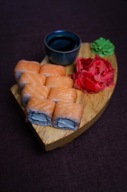 Sushi rolls wasabi pickled ginger on wooden plate dark background