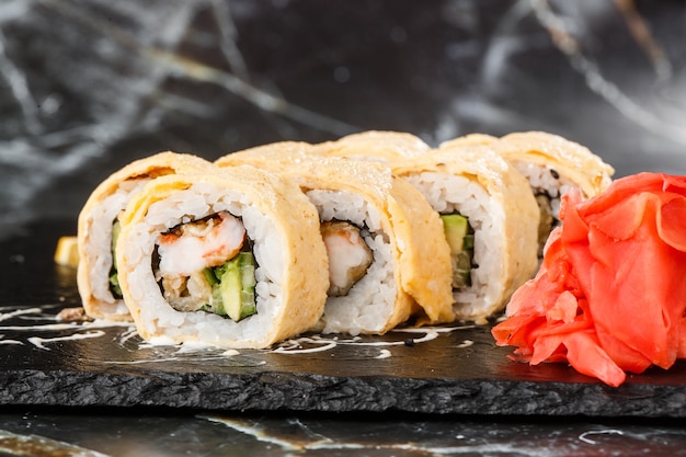 Sushi Rolls with avocado, eel, cucumber and cream cheese inside on black slate isolated on black marble background. California rolls covered on omelet Sushi menu. Horizontal photo.