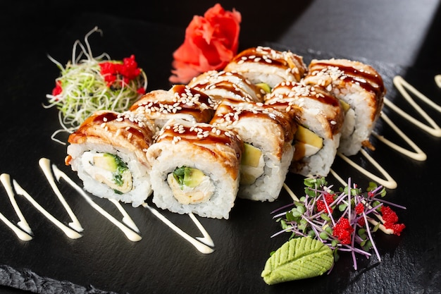 Photo sushi rolls with cucumber, avocado, eel, omelet and cream cheese inside on black