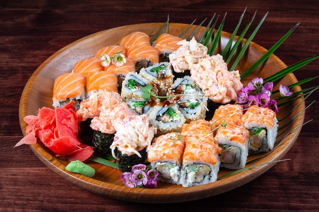 Sushi and rolls with sauce and spices on a wooden plate with green leaves. Traditional oriental dish