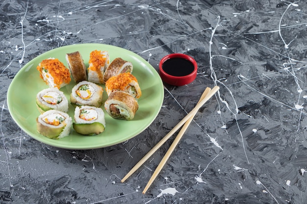 Sushi rolls with soy sauce placed on a green plate with chopsticks . 