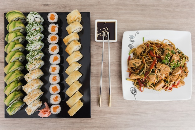 Sushi rolls with yakisoba and soy sauce on a wooden table