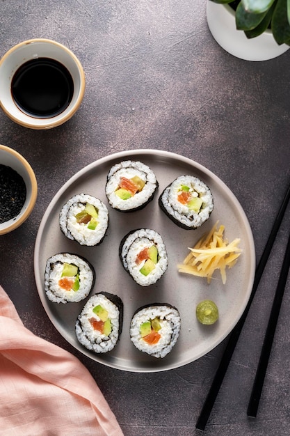 Sushi on round plate with chopsticks soy sauce ginger Homemade rolls with salmon avocado and cucumber