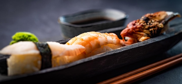 Sushi sashimi set with shrimps and soy sauce served with wooden chopsticks and wasabi on black table...