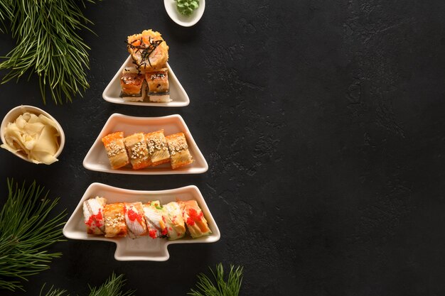 Sushi set served on plate as Christmas tree with Xmas decoration on black background.