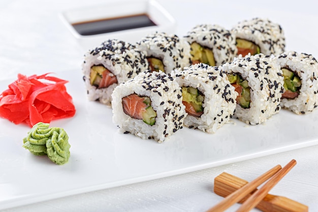 Sushi with salmon on a white plate with wasabi ginger soy chopsticks on a white background