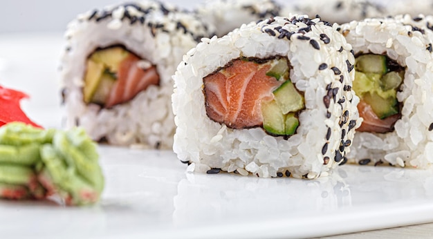 Sushi with salmon on a white plate with wasabi ginger soy chopsticks on a white background