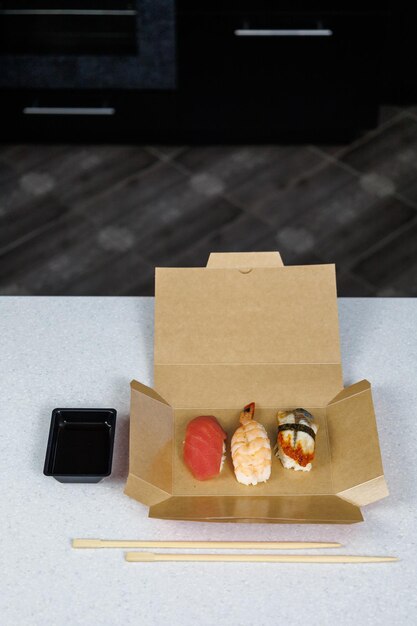 Sushi with tuna shrimp and eel lies in a cardboard box on the table in the kitchen Fast food concept