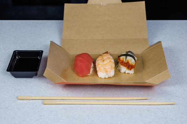 Sushi with tuna shrimp and eel lies in a cardboard box on the table in the kitchen Fast food concept