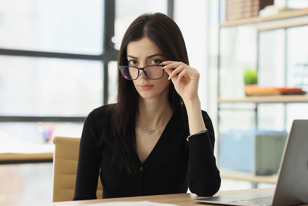 Suspicious woman with glasses sits at desk in office