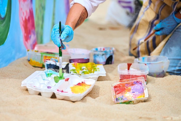 Svetlogorsk Russia  08152021  Woman painter in blue gloves choosing colors to paint picture with paint brush Mixing paints of different colors Acrylic painting outdoor art performance festival