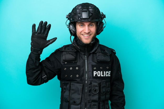 SWAT caucasian man isolated on blue background saluting with hand with happy expression