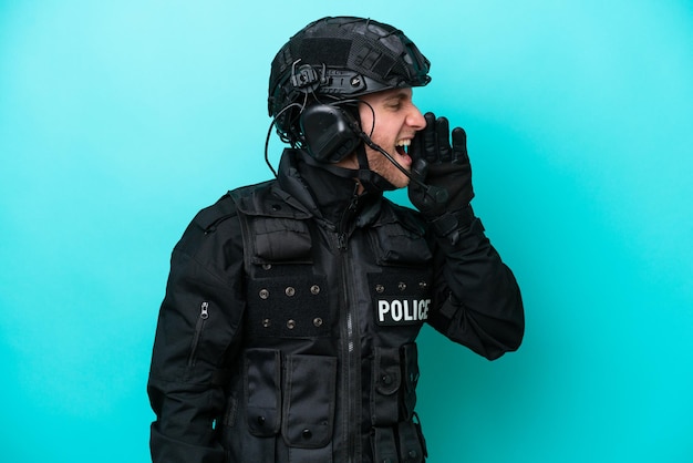 SWAT caucasian man isolated on blue background shouting with mouth wide open to the lateral