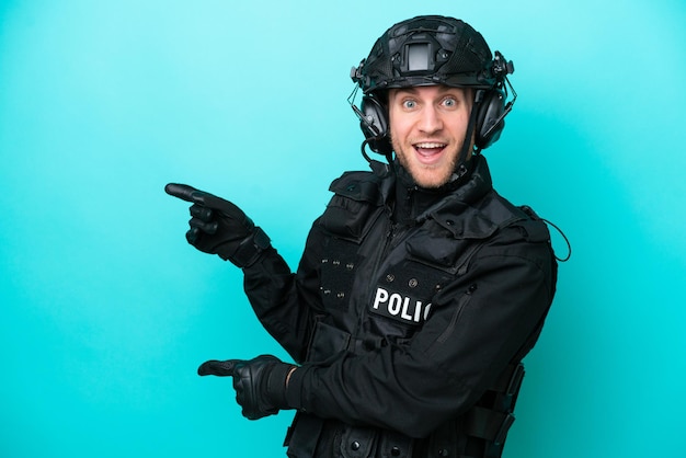 SWAT caucasian man isolated on blue background surprised and pointing side