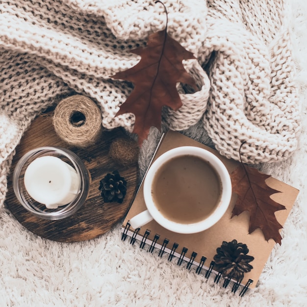 Sweaters and cup of tea with notebook, candle and knitting clothes