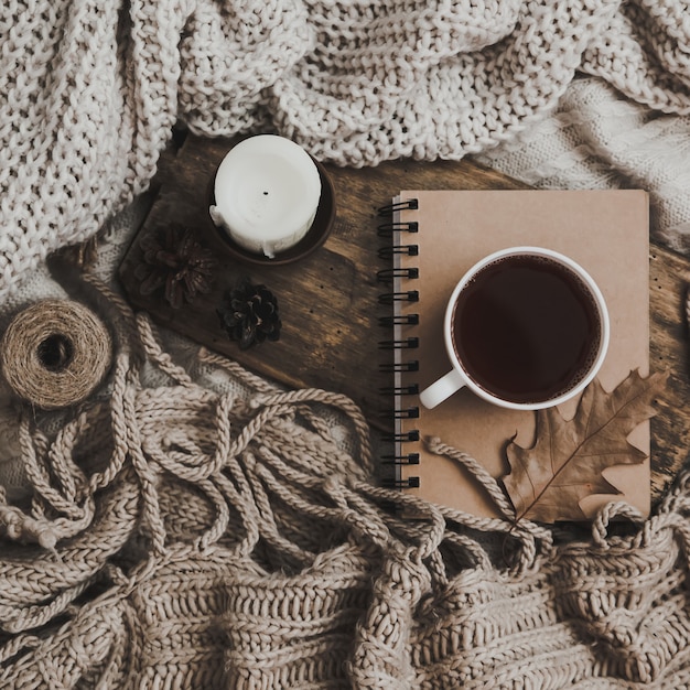 Sweaters and cup of tea with notebook, candle and knitting clothes