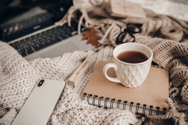 Sweaters and cup of tea with notebook, laptop and phone