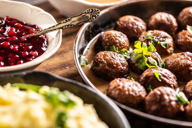 Photo swedish food kottbullar meatballs, served in a pan with mashed potatoes, parsley and cranberry sauce.