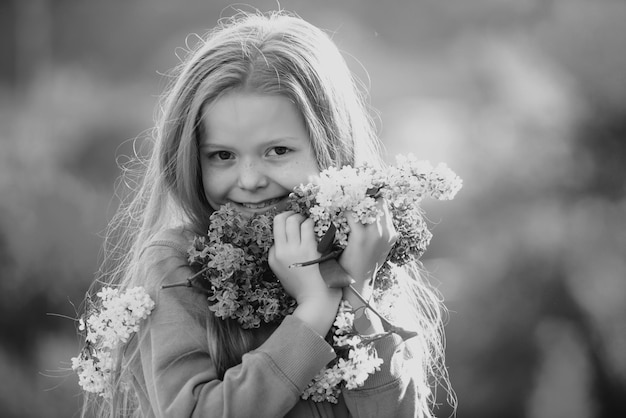 Sweet adorable young little lady in the garden with long fair hair being excited to get a bouquet of