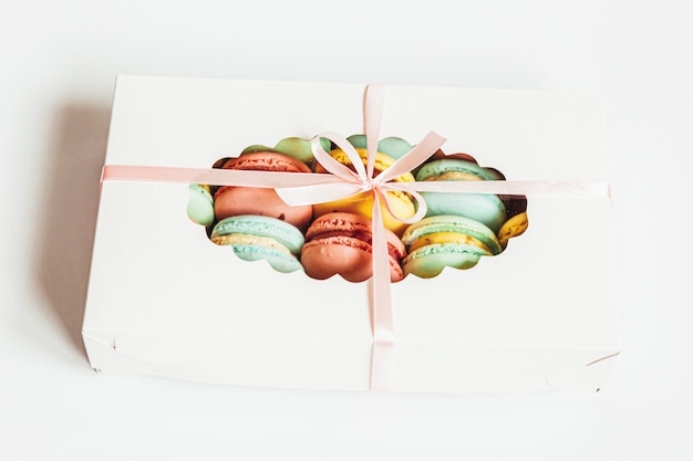 Sweet almond colorful pink blue yellow green macaron or macaroon dessert cake in gift box isolated on white table. French sweet cookie. Minimal food bakery concept. Flat lay top view, copy space