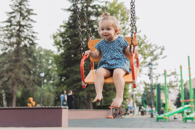 Sweet baby in a blue dress swings on a swing on a playground in the park lifestyle