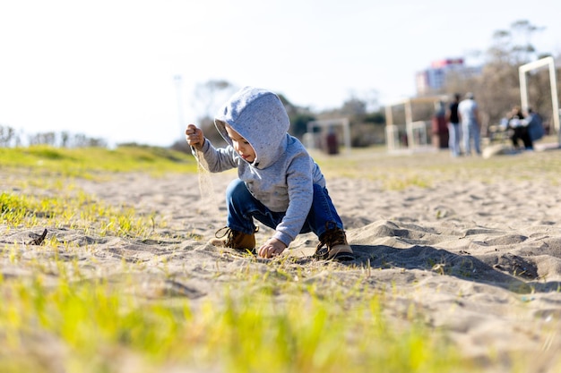 Sweet baby boy in hoodie and jeans playing in the sand Activity with toddler