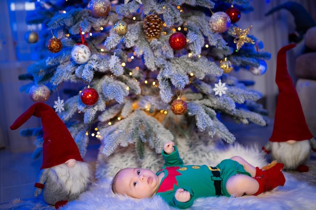 Sweet baby lying on the floor in a costume of elf Baby near the fur tree at the new year Side view