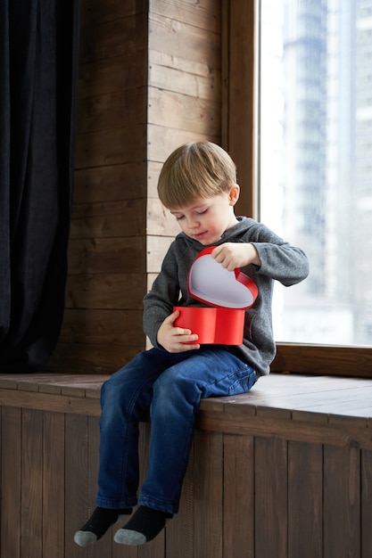 Sweet boy holding red present with hearts on white background valentines day or kids healthcare medi...