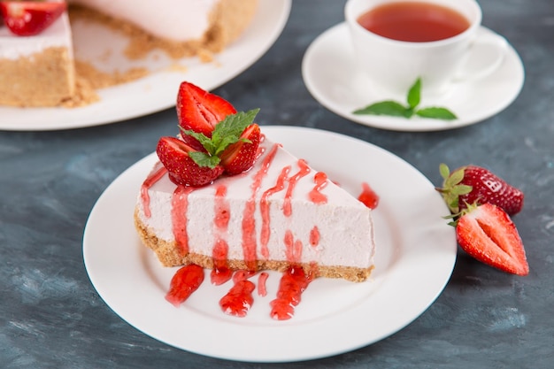 Sweet breakfast tea and delicious cheesecake with fresh strawberries and mint homemade recipe without baking on dark blue stone table Copy space