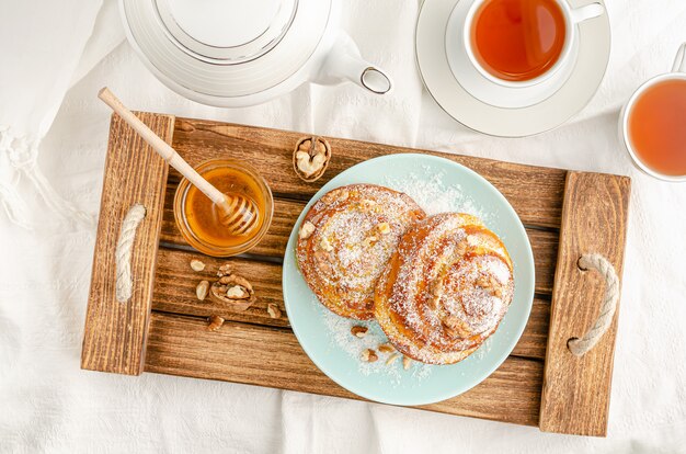 Sweet buns with walnuts, grated coconut and honey on a wooden tray