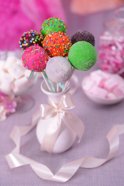 Sweet cake pops in vase on table on bright background