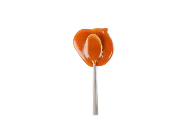 Sweet caramel sauce in spoon isolated on white background Melted liquid toffee Top view