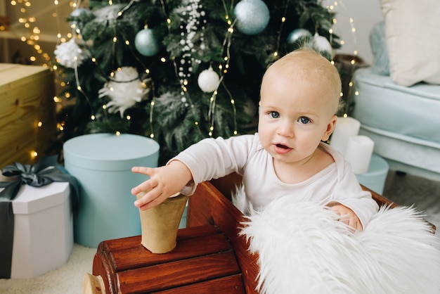 Sweet Caucasian baby sitting in a wooden toy train near decorated Christmas Tree