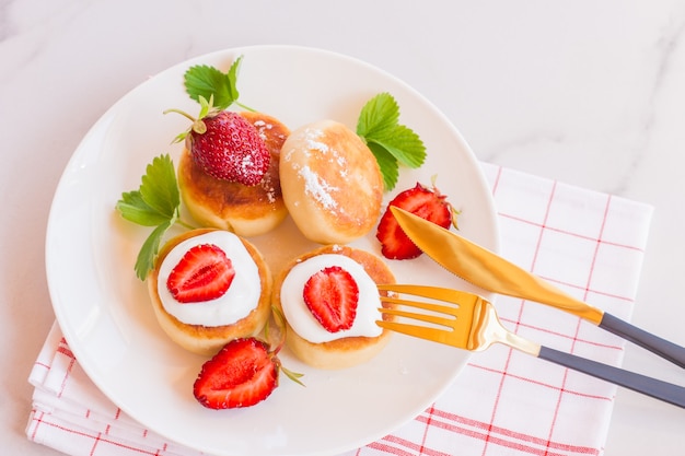 Sweet cheese pancakes on plate served with strawberries. Cottage cheese pancakes, syrniki, ricotta fritters, curd fritters. Top view or flat lay.