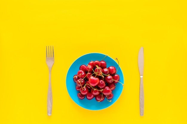 Sweet cherry in blue plate on yellow background