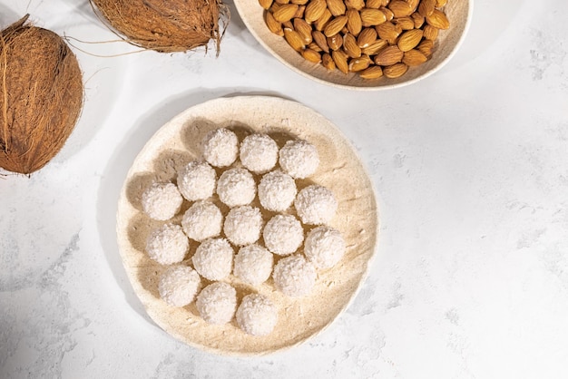 Sweet coconut candies in round plate, coconuts and almond nuts on background, close up with selective focus, banner with free space. High quality photo