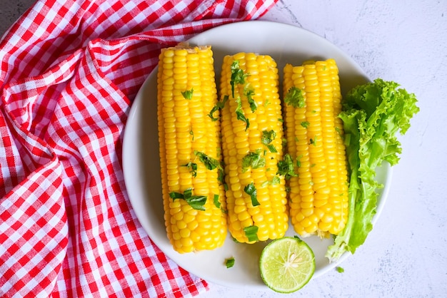 Sweet corn food with salad vegetable lime coriander and lettuce ripe corn cobs steamed or boiled sweetcorn for food vegan dinner or snack sweet corn cooked on white plate background