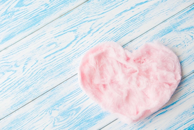 Sweet cotton candy in heart shape on blue wooden background. Copy space