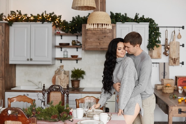 Sweet couple of young lovers posing at the decorated kitchen on christmas morning