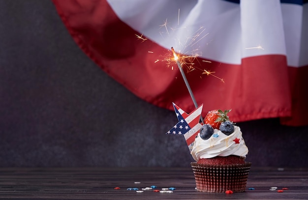 Sweet cupcake with blueberries and strawberry and sparkler over usa flag background