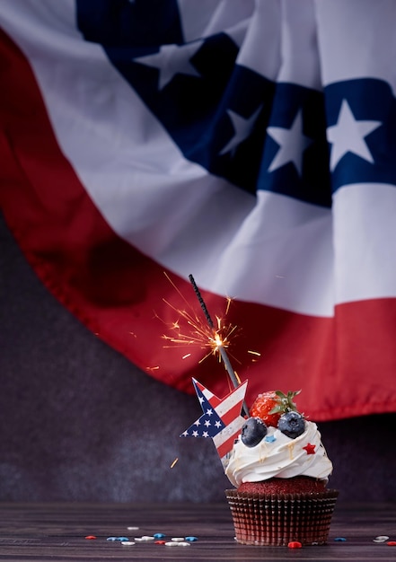 Sweet cupcake with blueberries and strawberry and sparkler over usa flag background