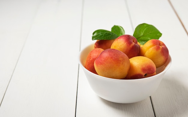 Sweet delicious apricot on dark bowl white wood table summer fresh fruit