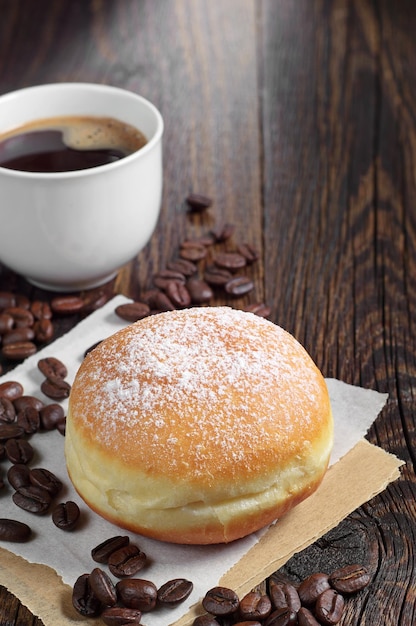 Sweet donut sprinkled with powdered sugar and coffee cup on wooden table