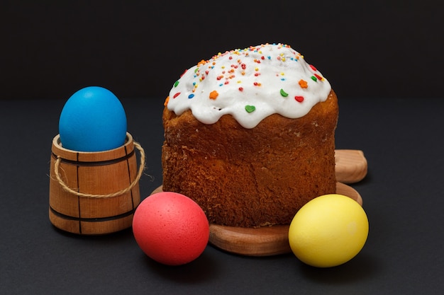 Sweet Easter cake on a wooden cutting board and colorful Easter eggs with the black surface