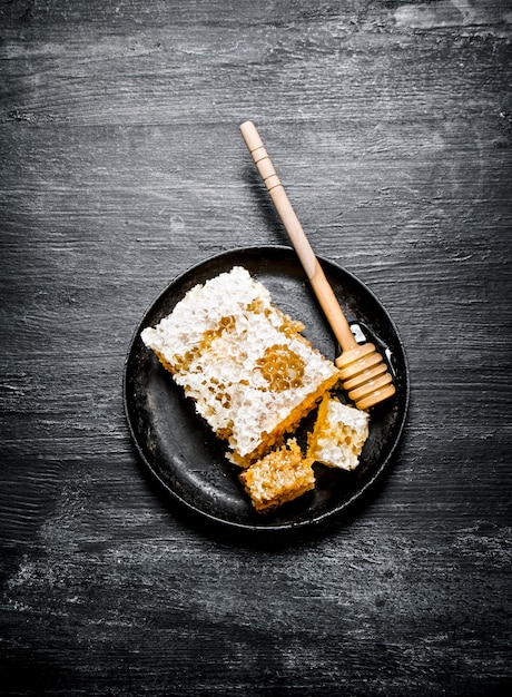 Sweet flavored honey in the comb with a spoon in the pan. On black rustic background.