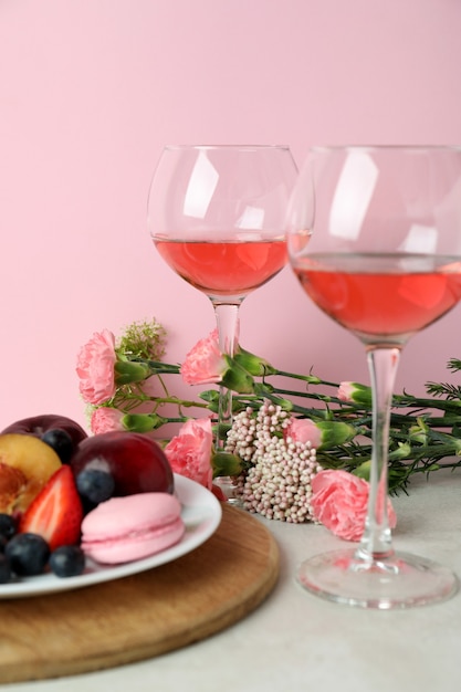 Sweet food, wine and flowers against pink background