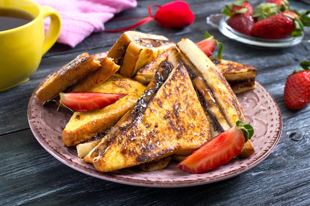 Sweet french toasts with banana, chocolate, strawberries on a wooden surface. Tasty breakfast